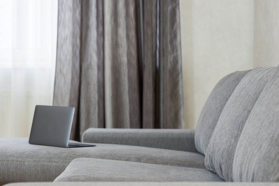 Modern flat interior with open netbook placed on couch with pillows against window with gray curtains
